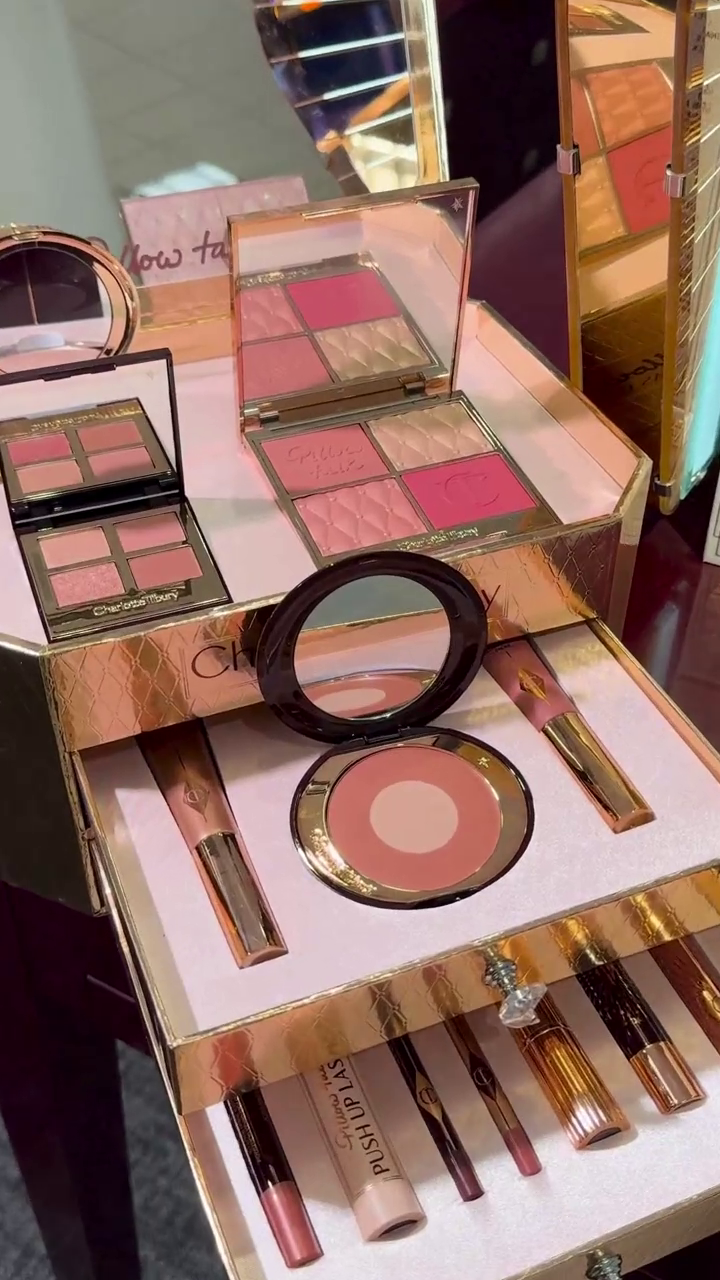 Luxurious Charlotte Tilbury Makeup Collection, Featuring Soft Pink Eyeshadows, Blushes, Lipsticks, and a Highlighter, Presented in Elegant Rose-Gold Packaging with a Sleek Vanity Display for Effortless Glam.