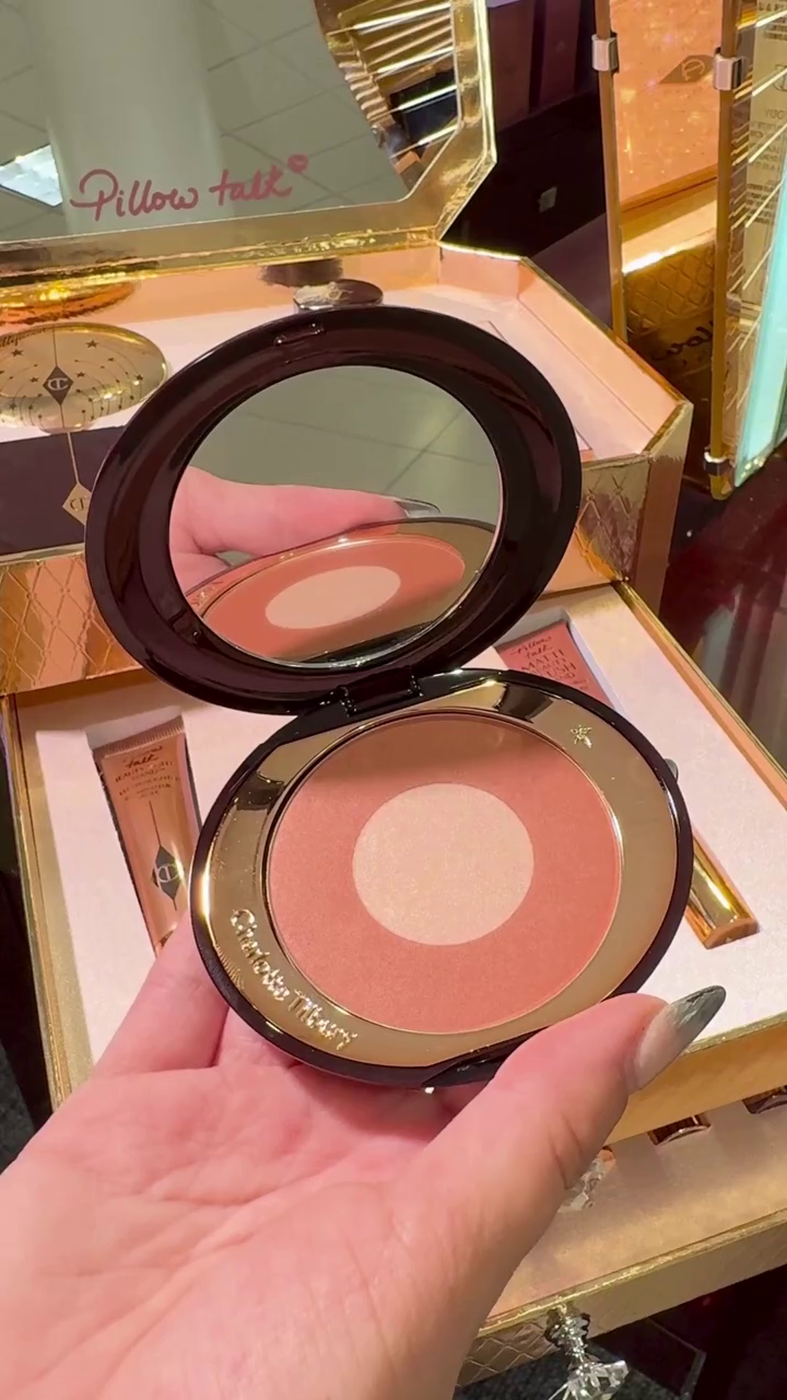 Luxurious Charlotte Tilbury Makeup Collection, Featuring Soft Pink Eyeshadows, Blushes, Lipsticks, and a Highlighter, Presented in Elegant Rose-Gold Packaging with a Sleek Vanity Display for Effortless Glam.