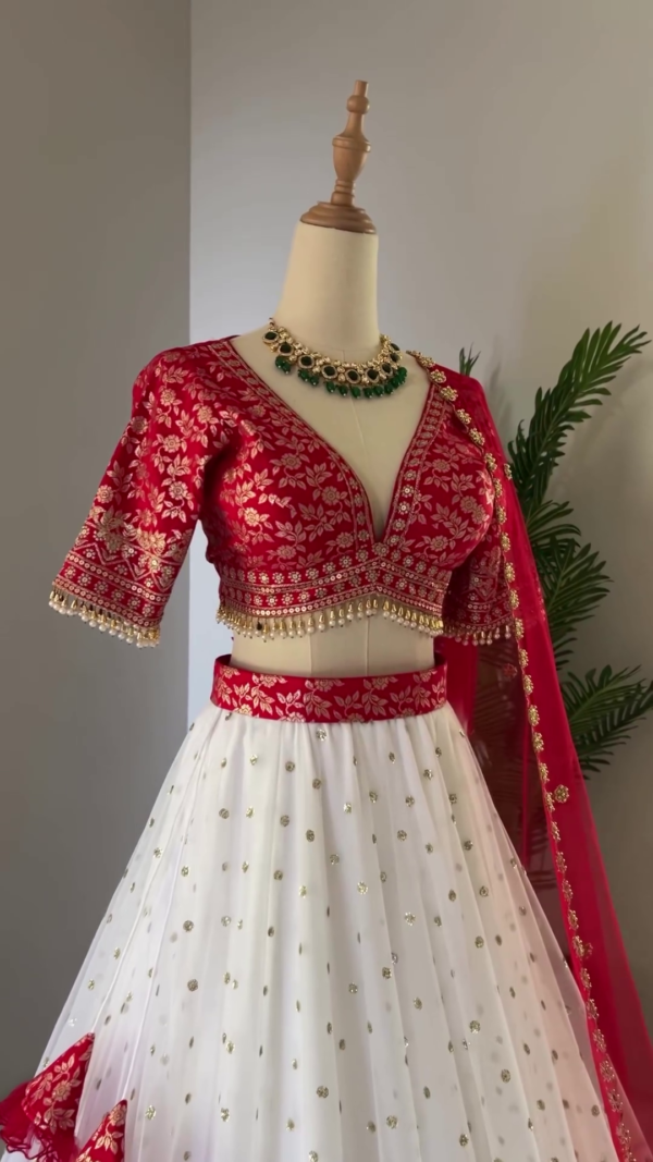 Red and White Bridal Lehenga Choli Set Featuring Deep V-Neck Embroidered Blouse, Flowy White Skirt with Gold Polka Accents and Rich Brocade Border, Paired with Sheer Red Dupatta Adorned with Floral Embellishments and Tassel Details – Perfect for Weddings and Grand Celebrations - Image 2