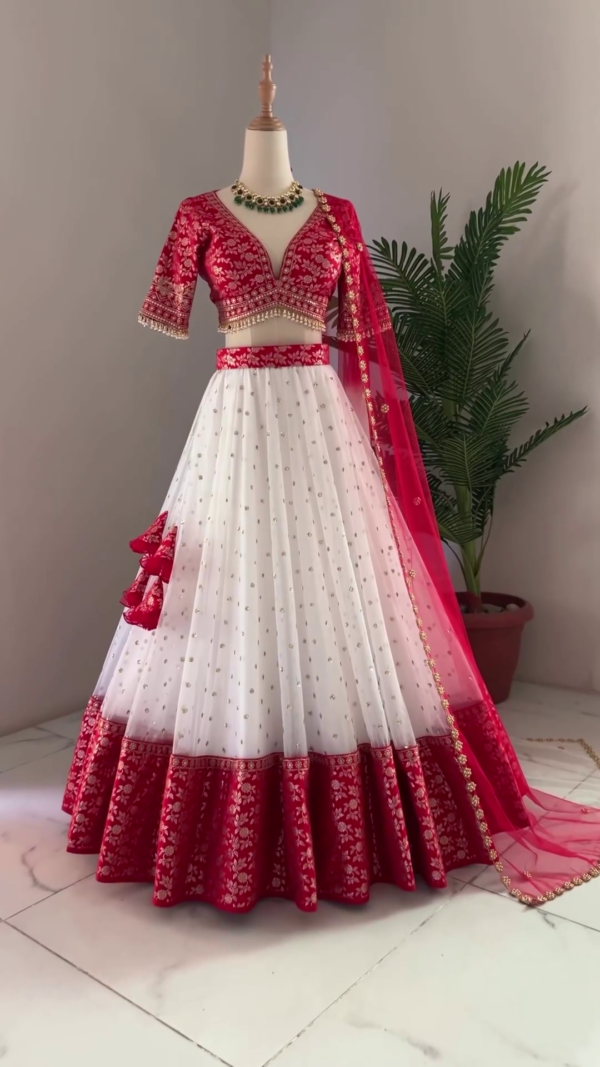 Red and White Bridal Lehenga Choli Set Featuring Deep V-Neck Embroidered Blouse, Flowy White Skirt with Gold Polka Accents and Rich Brocade Border, Paired with Sheer Red Dupatta Adorned with Floral Embellishments and Tassel Details – Perfect for Weddings and Grand Celebrations